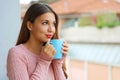 Close up of young woman with warm sweater enjoying hot drink in the morning at home on balcony outdoors