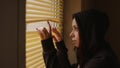 Close up of young woman watching through window blinds at home. Portrait of curious female observing through window Royalty Free Stock Photo