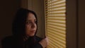 Close up of young woman watching through window blinds at home. Portrait of curious female observing through window Royalty Free Stock Photo