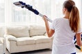 Close up of young woman in white shirt holding in hands wireless vacuum cleaner while cleaning in living room at home, back view. Royalty Free Stock Photo