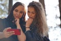 Close up of young women taking selfie on smartphone in wood. Pretty females photographing on mobile phone.