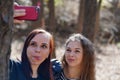 Close up of young women taking selfie on smartphone in wood. Pretty females photographing on mobile phone.