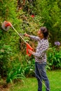 Close up of young worker wearing transparent glasses protection and holding a lawn trimmer mower cutting some bushes, in Royalty Free Stock Photo