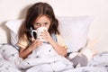 Close upportrait of child girl drinking hot tea to recover from flu, wearing pajama and scarf, dark haired child with mug in hands Royalty Free Stock Photo