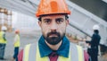 Close-upportrait of serious guy wearing safety helmet and west standing in construction site