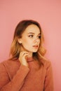 Close vertical portrait of a cute lady in a sweater looking to the side, isolated on a pink background