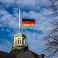 Close view on German Flag at Halfmast, auf Halbmast, on the tower roof of Castle Karlsruhe, blue sky behind. Germany Royalty Free Stock Photo