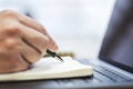 man's hand writing down notes in a notepad on a laptop, against a hazy backdrop Royalty Free Stock Photo