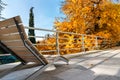 Close view of modern wooden empty lounger chair on patio balcony terrace against bright yellow orange autumn tree and