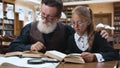 Wonderful portrait of pleasant happy grandfather and granddaughter which sitting in the library and reading books