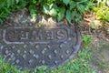 Close view of sewer manhole cover surrounded by mixed greenery, Royalty Free Stock Photo