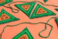 Close view of triangle crochet motifs in green and orange colors and a green crochet cord on orange background.