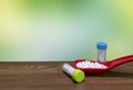 Close view of White pills in red spoon with Homeopathic medicine bottles on wood surface and green mix yellow background Royalty Free Stock Photo