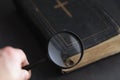 Closed ancient bible with gold cross with hand holding magnifying glass. Search for truth and meaning of life