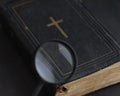 Closed ancient bible with gold cross viewed through magnifying glass. Search for truth, meaning of life. Religious book