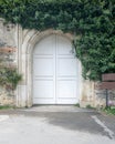 Closed arched white wooden door surrounded by green leaves on old grunge stone wall Royalty Free Stock Photo