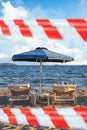 Closed beach with warning tape in Greece. Sand, beach lounger and umbrella. Delayed vacation concept