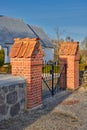 A closed black iron gate between two red brick pillars at a park on a sunny summer day. Outdoor entrance to a home or