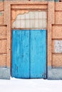 Closed blue painted door, pink plaster on wall, grunge background, winter snowy street Royalty Free Stock Photo