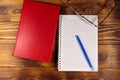 Closed book, eyeglasses, notepad and pen on wooden background