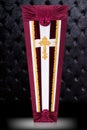 Closed bordo and white coffin covered with cloth on gray luxury background. Coffin with gold Church cross.