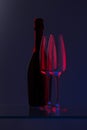 Closed bottle of champagne with two empty glasses. Blue-red color. Royalty Free Stock Photo