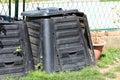 Closed broken old dirty full black plastic compost bins next to metal fence surrounded with uncut grass Royalty Free Stock Photo