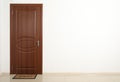 Closed brown door with welcome mat in white wall