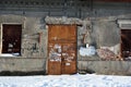 Closed brown painted door with torn ads paper in which recognizable only separate letters, boarded up windows