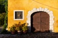 Closed brown wooden entrance door with barred window on yellow wall of ancient medieval village. Strassoldo Italy. Royalty Free Stock Photo