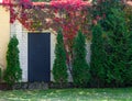 A door in a white brick wall among green trees and bushes with red leaves. Royalty Free Stock Photo