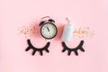 Closed decorative eyes, two pills, white bottle, black alarm clock and gold stars confetti on pink background. Concept Insomnia, Royalty Free Stock Photo