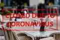 Closed Due To Quarantine - sign on the background of an empty cafeteria or restaurant tables with chairs on street