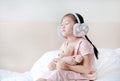 Closed eyes little Asian child girl wearing winter earmuffs and embracing teddy bear while sitting on the bed at home Royalty Free Stock Photo