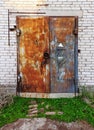 Closed flaps of old metal rusty locked gates in a wall made of white brick and concrete