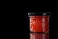 Closed glass jar with red salmon caviar. Black background. Free space for an inscription Royalty Free Stock Photo