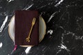 Closed Holy Bible Book on top of empty plate with golden fork on dark background with copy space