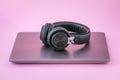 Closed laptop and earphones. Metallic notebook and black portable headphones on a pink background. Entertainment concept of