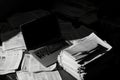 A closed laptop sits among piles of newspapers scattered on the desk. The dim lighting Royalty Free Stock Photo