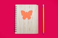 Closed notebook bound in babmouk with an orange butterfly ornament on a pink background and a yellow pencil Royalty Free Stock Photo