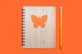 Closed notebook bound in bamboo with a butterfly ornament on an orange background and a yellow pencil Royalty Free Stock Photo