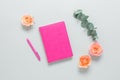 Closed pink notebook with a pen on a gray background decorated with roses and a branch of eucalyptus. Blogger or freelance