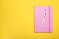 Closed pink notebook and pen on yellow background, top view. Space for text Royalty Free Stock Photo