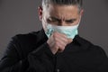 Closed portrait of man with surgical mask coughing in studio on gray background, healthcare concept