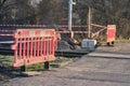 Railway tracks under construction crossing a road. Reflection orange-red-white barriers and a warning tape.