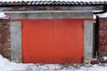 Closed red metal gate on a gray old wall of an outside garage in white snow Royalty Free Stock Photo