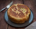 The closed round home-made cake lies on a gray plate, on a wooden table.