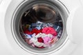 Closed round washing machine door with rotating garments inside. Focus in the center of dirty laundry and washing Royalty Free Stock Photo