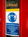 A closed shop with Covid-19 social distancing warning notice in the door window.