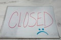 Closed sign on dry erase board with a sad face economic closure